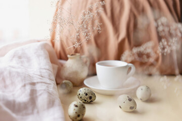 Easter cozy still life composition with qual eggs, cup of tea and beige cloth. Morning teatime