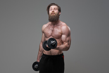 Stylish sportsman with dumbells staying in gray background