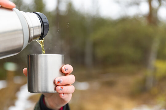 Youg beautifull women pouring beverage from termos to cup in a cold raini day. Healthy living and hiking.