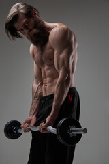 Fototapeta na wymiar Topless sportsman holding heavy barbell looks down in gray background