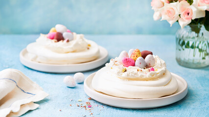 Obraz na płótnie Canvas Meringue nest cake with colorful chocolate eggs, buttercream frosting on light blue background with copy space. Selective focus. Food ideas for kids. Easter cake. Spring love feast concept. Close up.
