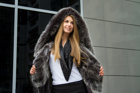 Portrait of a beauty fashion model girl in a fur coat posing on a city street. Beautiful Luxury Winter Woman. Portrait of an attractive smiling blonde in outer clothing