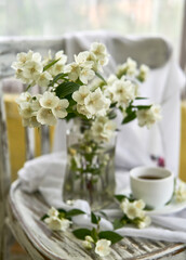 Fototapeta na wymiar Jasmine flowers in a glasse vase. Stillife with jasmine and cup of coffee.
