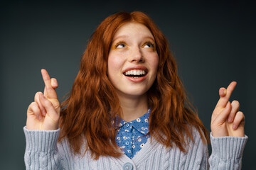 Young ginger happy woman holding fingers crossed for good luck