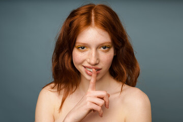 Fototapeta premium Shirtless smiling woman with makeup showing silence gesture at camera