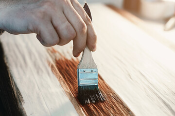 A working cabinetmaker holds a brush in his hand and paints a wooden surface. A trace of paint on a...