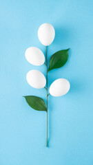 Twig with white eggs and green leaves on a blue background. Minimal creative concept for Easter