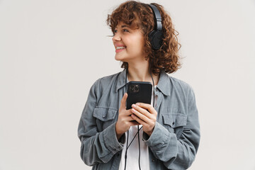 Fototapeta premium Young ginger joyful woman listening music with headphones and cellphone