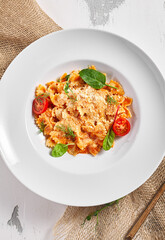 Farfalle pasta food on white table. Pasta restaurant plate with basil leaf and tomato, red tomato sauce. Delicious italian pasta.