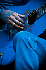 close up shot of a hand of a busker painted in blue playing a blue painted guitar.