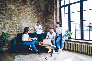 Skilled male and female millennial students watching video on laptop computer while e learning in coworking space,crew of diverse hipster guys analyzing information from web page and education reports