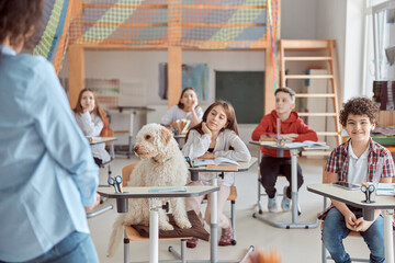Happy mixed kid pupils in elementary school lesson with a dog in center