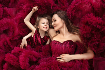 mother and daughter in the image of the queen and princess dresses Marsala colors lie together, top view