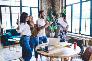 Happy multiracial coworkers cheering each other around table