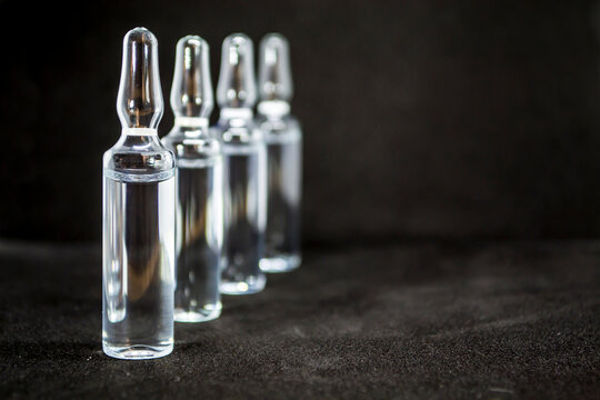 Glass medical ampoule vial for injection. Medicine is liquid sodium chloride with of aqueous solution in ampulla. Close up. Bottles ampule multicolor on background color and water. Human plasma.
