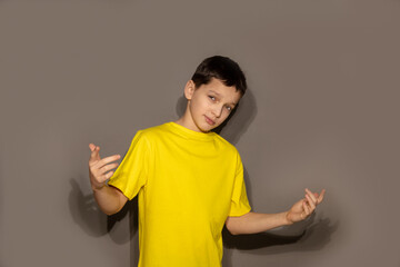 Young cheerful man teenager boy in stylish yellow t-shirt dancing happily on gray background