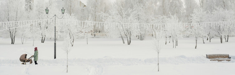 Winter city park in Russia, mom with a stroller is walking in the park. Banner