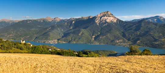 Serre-Poncon Lake and Grand Morgon Peak in summer with view on Savines-le-Lac village and the chapel of Saint-Apollinaire. Hautes-Alpes, Alps, France