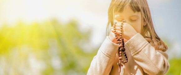 Little child girl praying with wooden rosary. Free copy space.