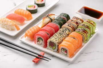 Various sushi rolls, soya sauce and chopsticks on a white stone background. Traditional Japanese food. Asian food