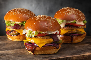 Three yummy juicy hamburgers with double cutlet and cheese on a wooden table. Grilled chicken...
