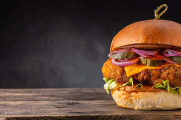 Big yummy chicken burger with cheese and pickles on a wooden board on a dark background. Hamburger...