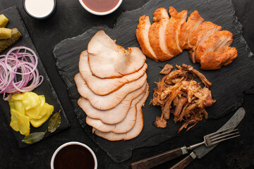 Sliced ​​smoked turkey fillet, smoked puilled pork and pickled vegetables set on a slate board,...