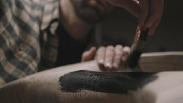 A furniture maker moves a brush over wood, paints a wooden table