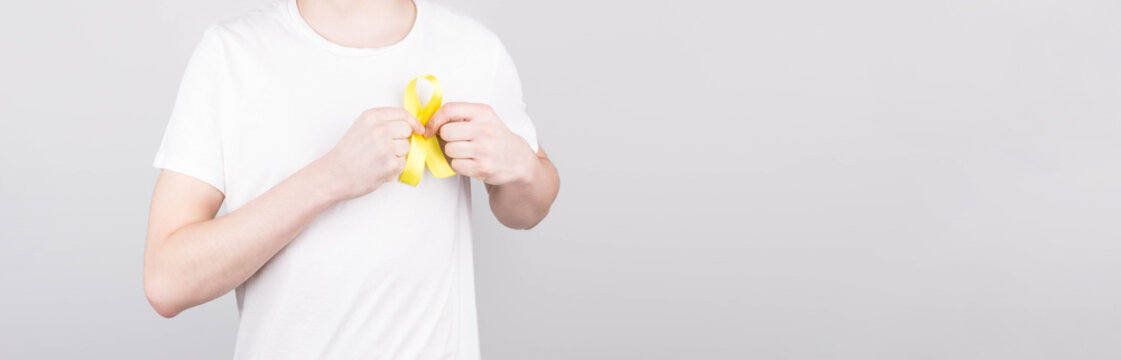 Young Man In White T-shirt Holding Yellow Ribbon Awareness Symbol For Suicide, Sarcoma Bone Cancer, Bladder Cancer, Liver Cancer And Childhood Cancer Concept. Health Care. Copyspace.