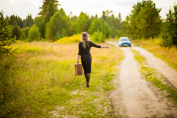 Obraz premium blonde girl in black dress with suitcase catches car, selective focus
