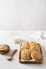 Homemade oatmeal cookies with banana, oats and nuts on a wooden tray and oats flakes on white background, side view, copy space. Healthy food. Oatmeat biscuits recipe