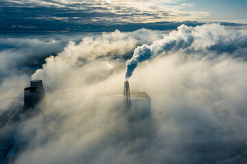 large clouds of white smoke cover power plant territory under bright sunlight on frosty winter day...