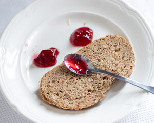 Slice of whole grain bread with two drops of red jam on a white plate making up a face