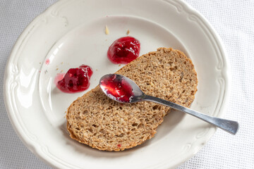Slice of whole grain bread with two drops of red jam on a white plate making up a face