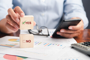 Close-up of hand holding a smartphone with the chart, graph report for the business and holding a wooden blocks for choice Yes or No. Space for text. Business and planning concept