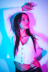 Party lifestyle in a nightclub with pink blue neon lights, portrait of a young brunette Caucasian woman in a woolen sweater