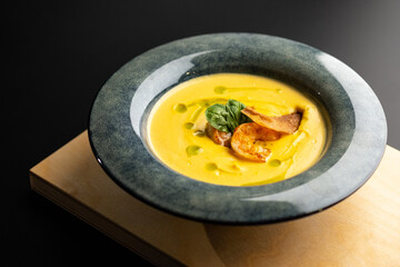 Cream pumpkin soup with grilled shrimp. Soup in a blue plate on a black background.