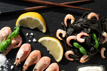 black pasta and shrimps with salt and lemon on a black background