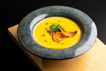 Cream pumpkin soup with grilled shrimp. Soup in a blue plate on a black background.