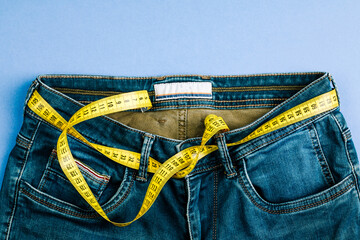 The concept of a healthy lifestyle and diet. Blue jeans with a yellow measuring tape instead of a belt.