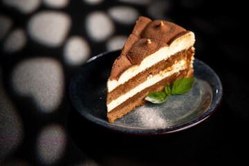 Italian sweet dessert tiramisu on a plate on a black background with mint leaf.