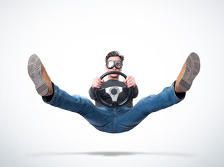 Surprised man in goggles in the air with a car steering wheel in his hands, on light background,...