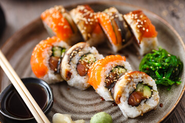 Sushi maki rolls with salmon, eel, avocado, cucumber on a plate with chopsticks, soy sauce, wasabi and ginger. Japanese traditional fish food closeup served for lunch in modern gourmet restaurant