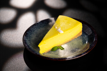 A piece of lemon sweet dessert on a plate on a black background.