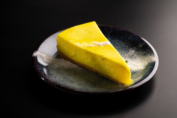 A piece of lemon sweet dessert on a plate on a black background.
