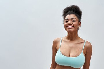 Obraz na płótnie Canvas Portrait of beautiful sexy young mixed race woman wearing blue underwear smiling at camera while posing isolated over light background