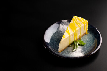 Sweet dessert on a plate on a black background. Classic cheesecake with yellow lemon syrup.