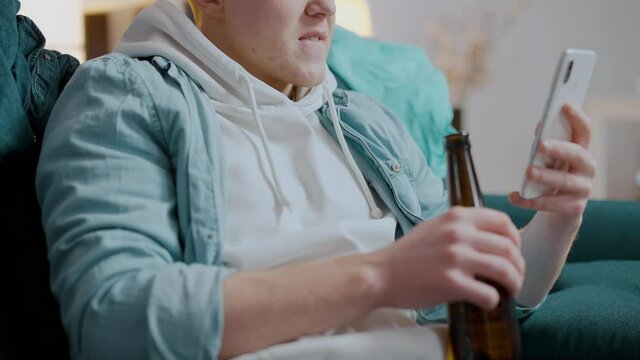 Pleased male drinking bottled beer, enjoying website photos with adult content