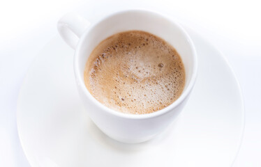 Cup of coffee with saucer with handle,  isolated on a white table. Seen obliquely from above. Focus on the froth of the coffee