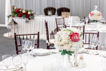 Fancy table set for dinner with flower composition in restaurant, luxury interior background. Wedding elegant banquet decoration and items for food arranged by catering service on white table.